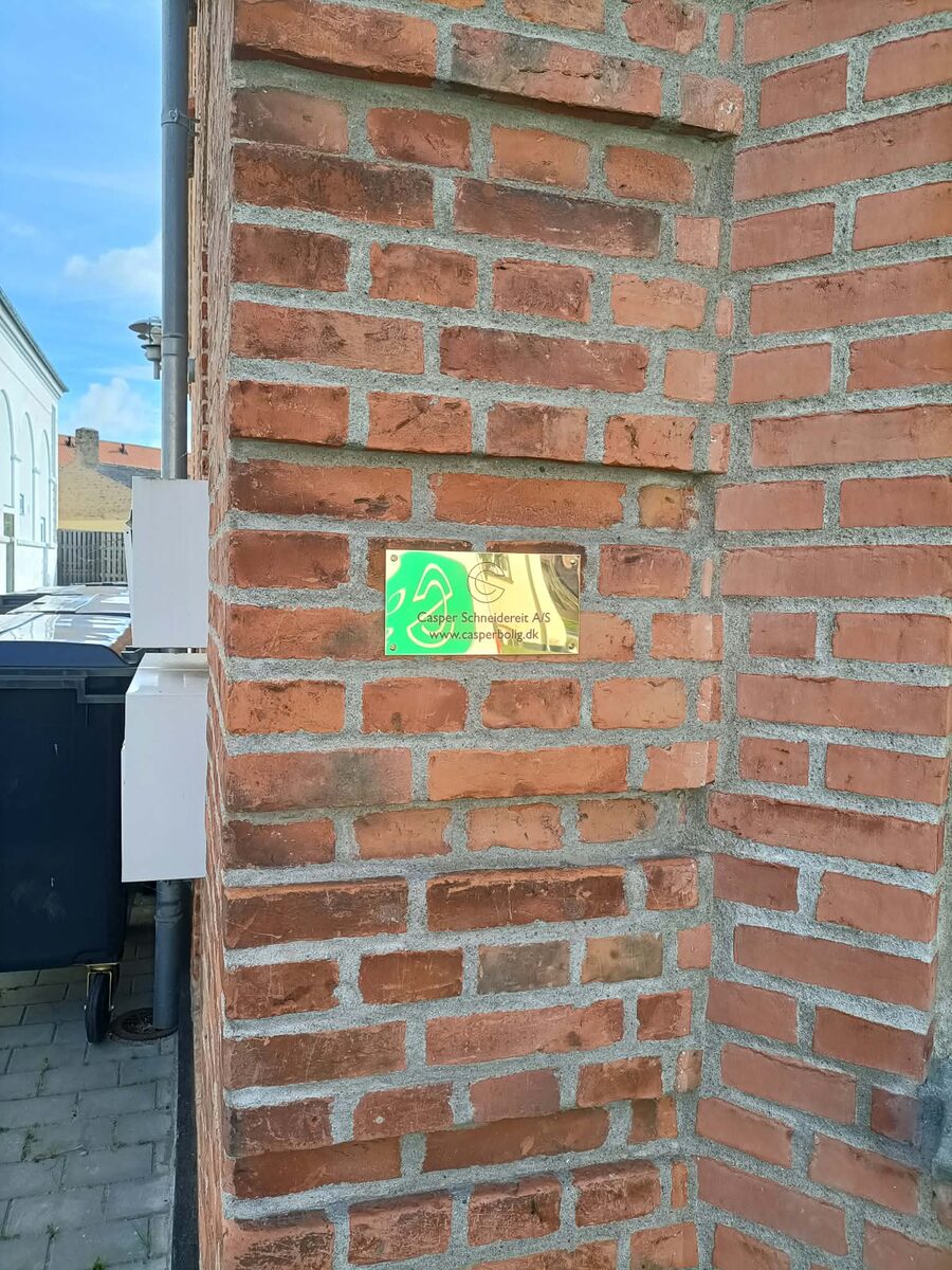 Nyt messingskilt med navn og webadresse på en rød murstensfacade